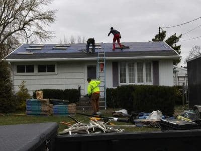Workers installing solar panels on a residential roof, with tools and materials in the foreground.
