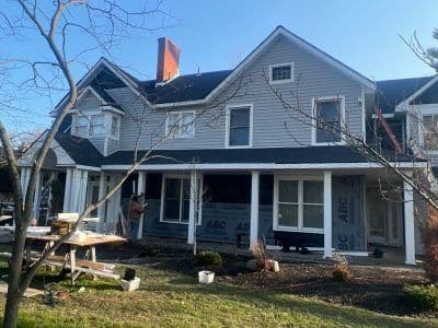 Renovated house exterior with scaffolding, tools, and trees in the yard on a sunny day.