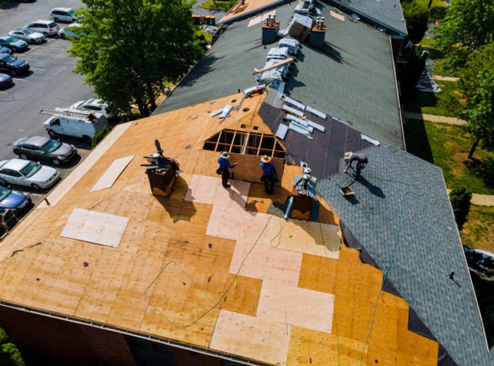 Roof renovation in progress, featuring workers installing new shingles on a building.