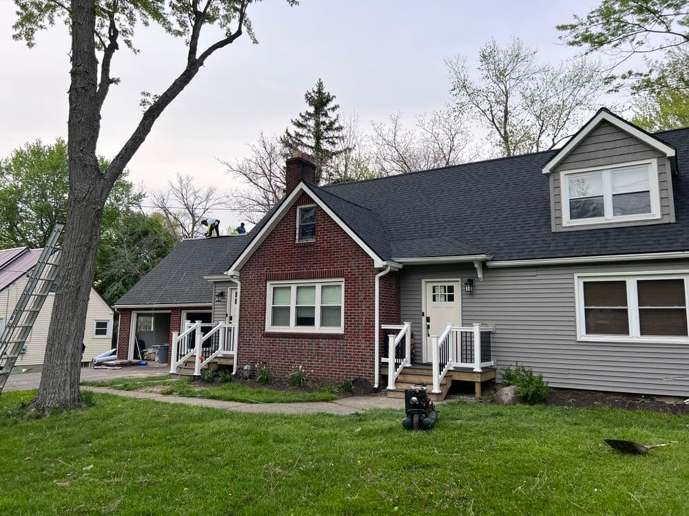 Home renovation with workers roofing a house, featuring brick and siding exterior.
