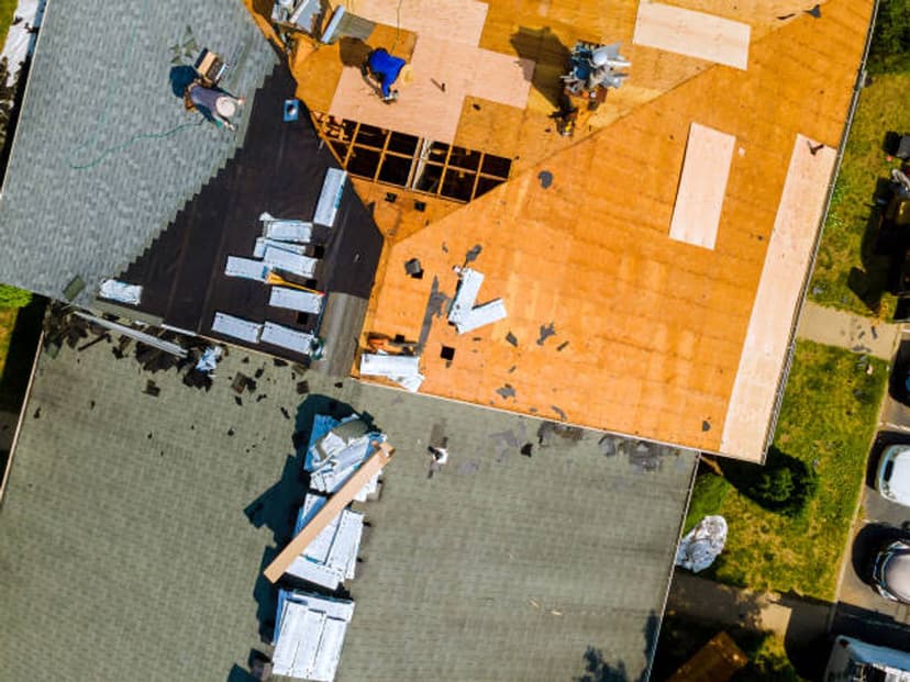 Aerial view of roofing work in progress on multiple homes with exposed plywood and materials.