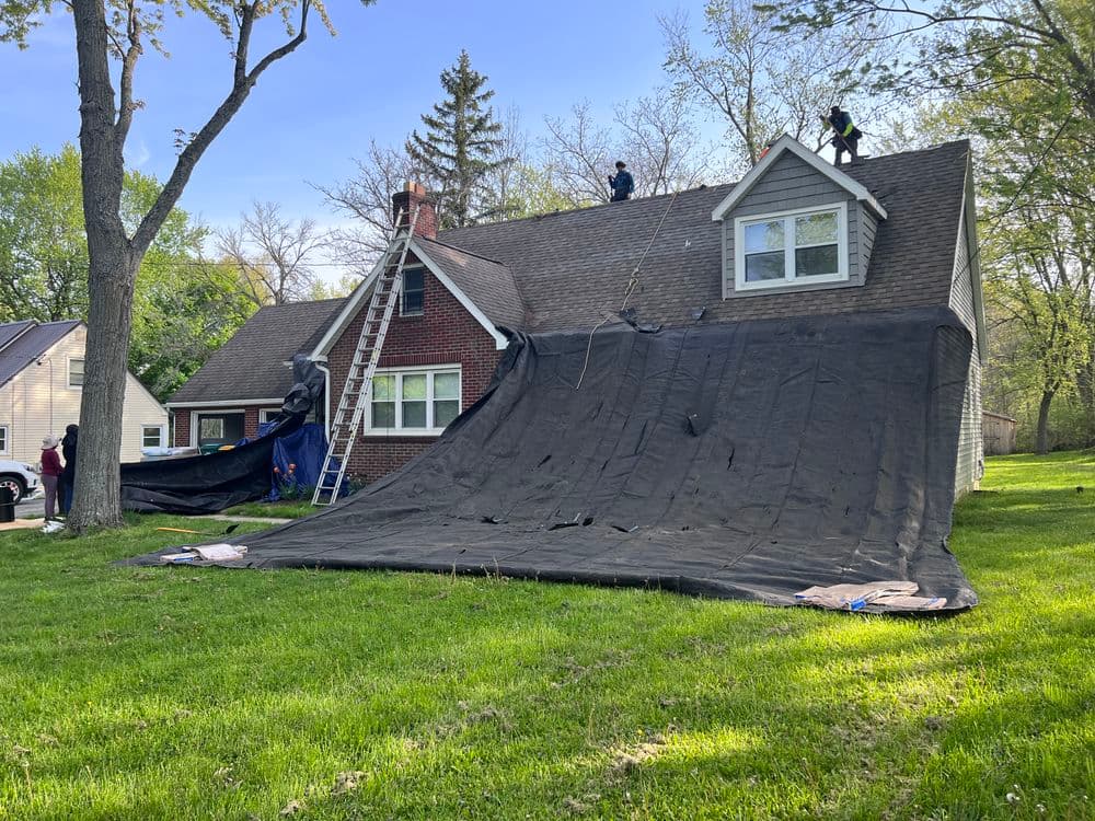 Roof repair crew applying tarp on residential home for protection during repairs.