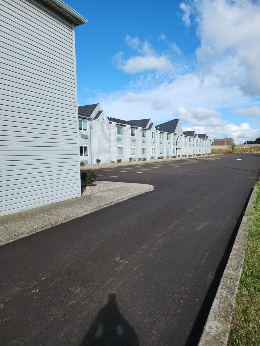 Modern white hotel buildings alongside a freshly paved parking area under a blue sky.