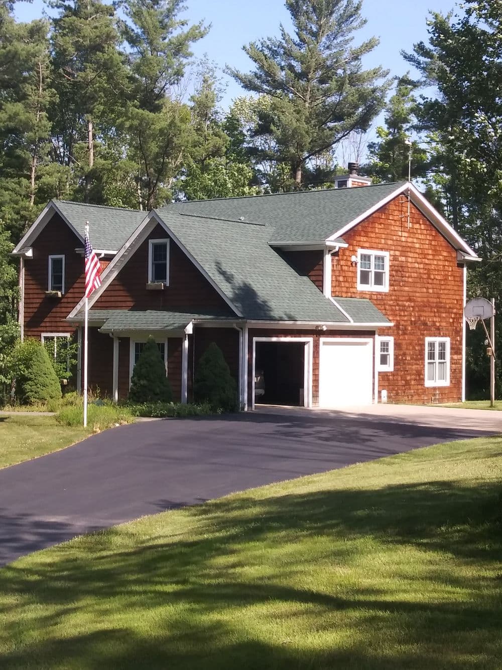 Charming two-story home with wooden siding, American flag, and lush green lawn.