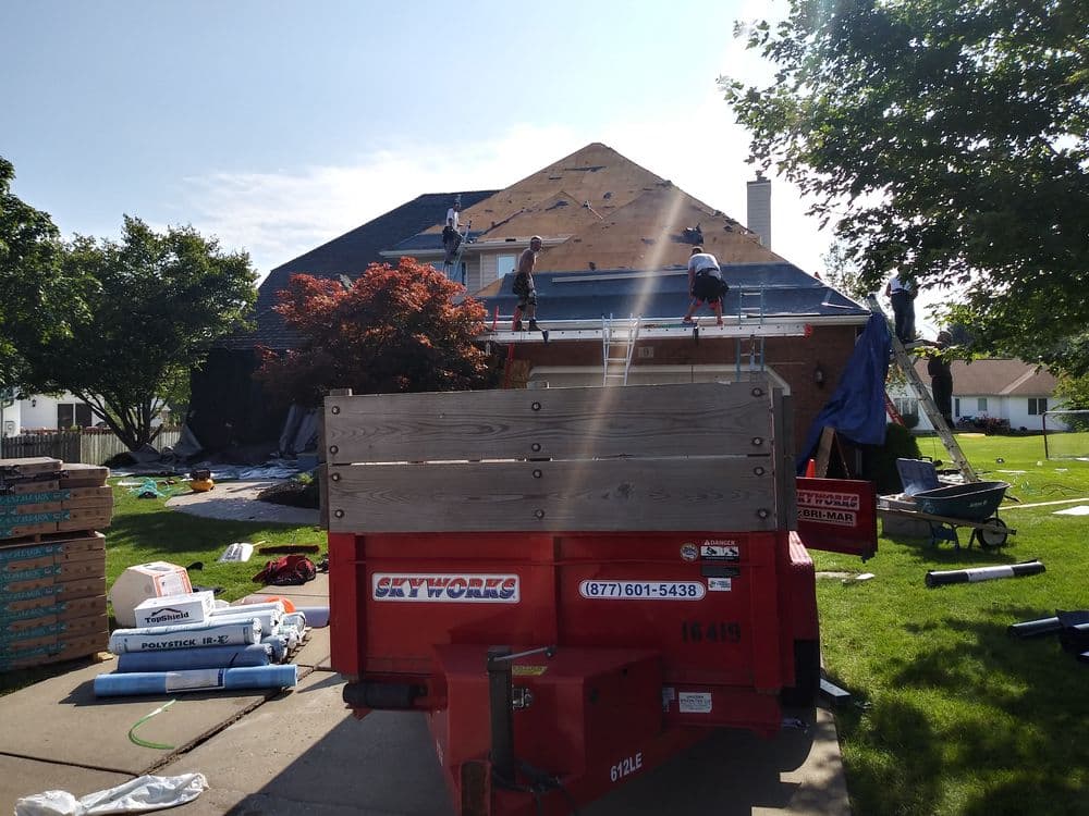 Roofing crew repairing residential home with tools and materials scattered in the yard.