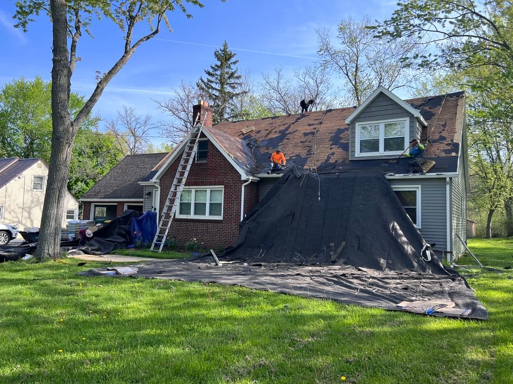 Roofing crew working on a house, with shingles removed and tarps on the ground for protection.
