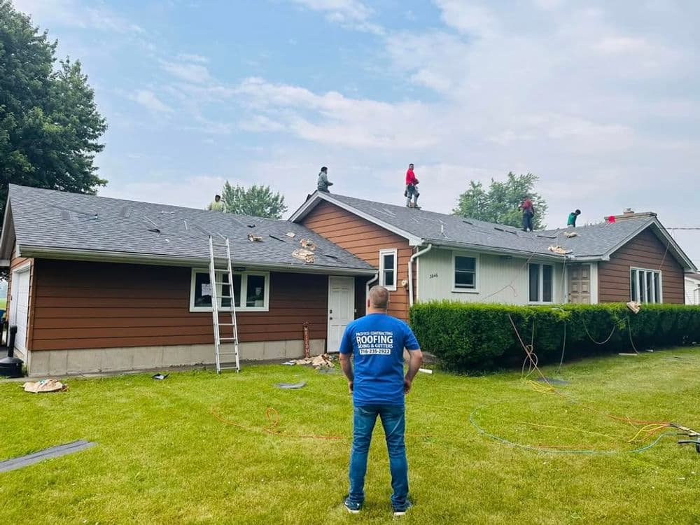Roofing crew working on a home, with a man overseeing the project from the yard.