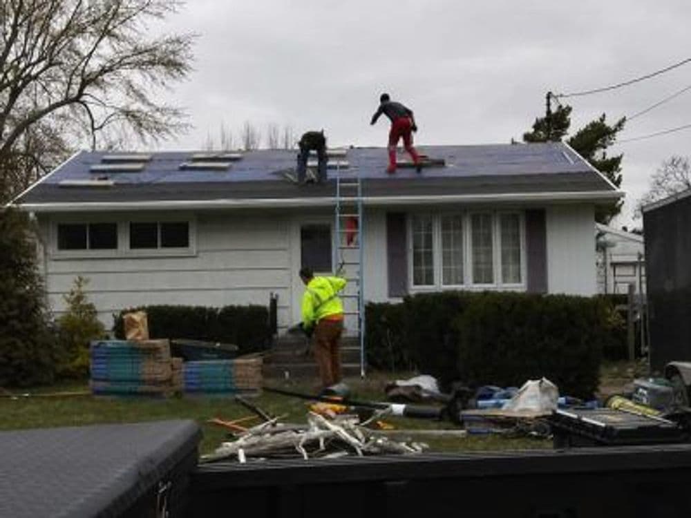 Workers installing solar panels on a residential roof with tools and materials in the yard.