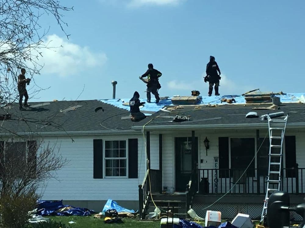 Workers installing a new roof on a residential home with tools and materials scattered around.