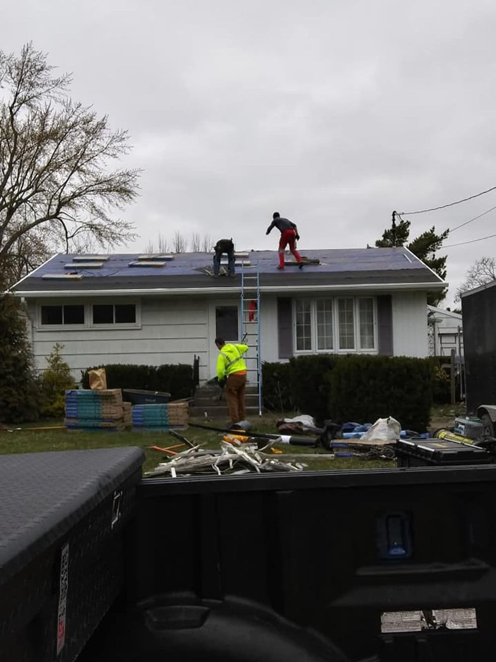Roof repair work in progress on a residential home, with workers and tools visible.