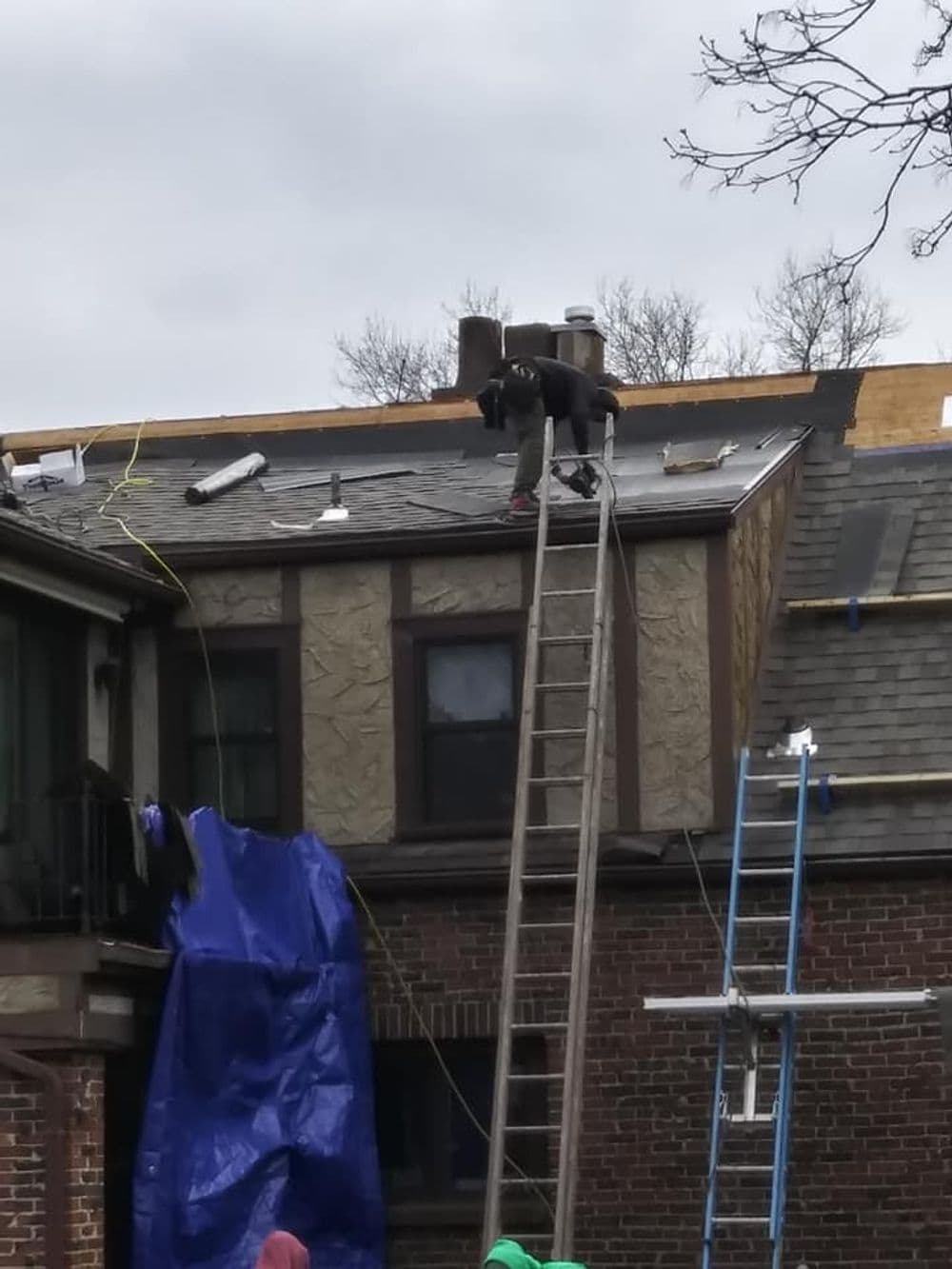 Worker repairing a roof with a ladder and blue tarp, showcasing home maintenance.