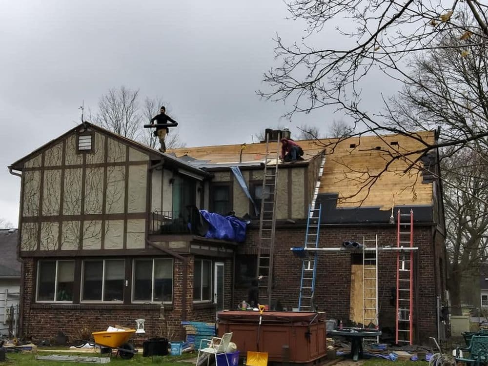 Roofing crew replacing shingles on a home's roof with tools and ladders visible.