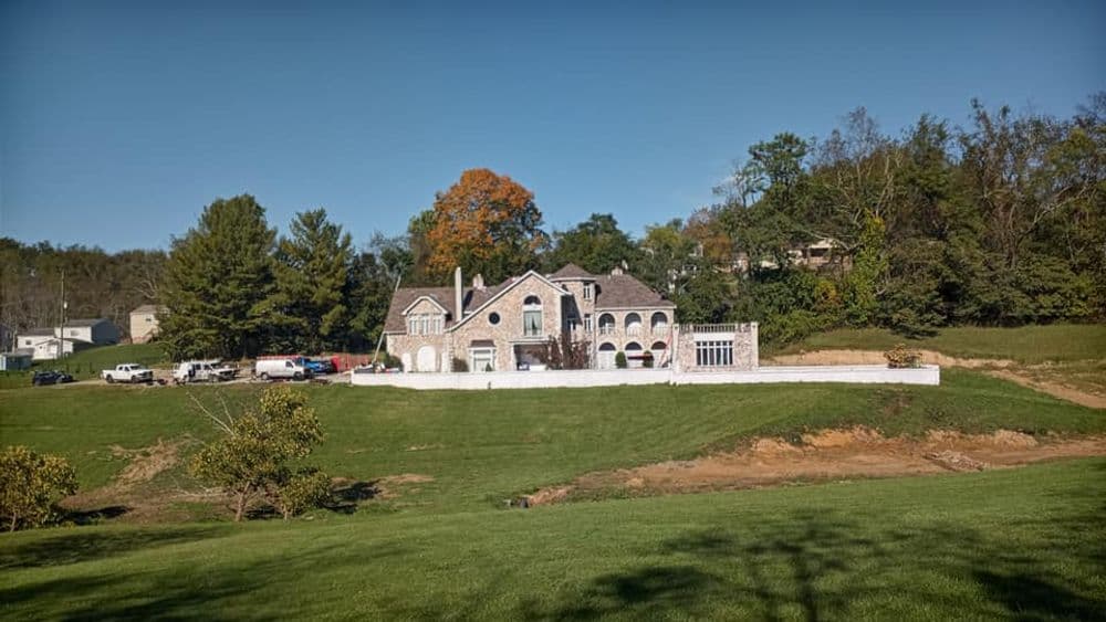 Elegant stone mansion set on a green landscape with trees and fields in the background.