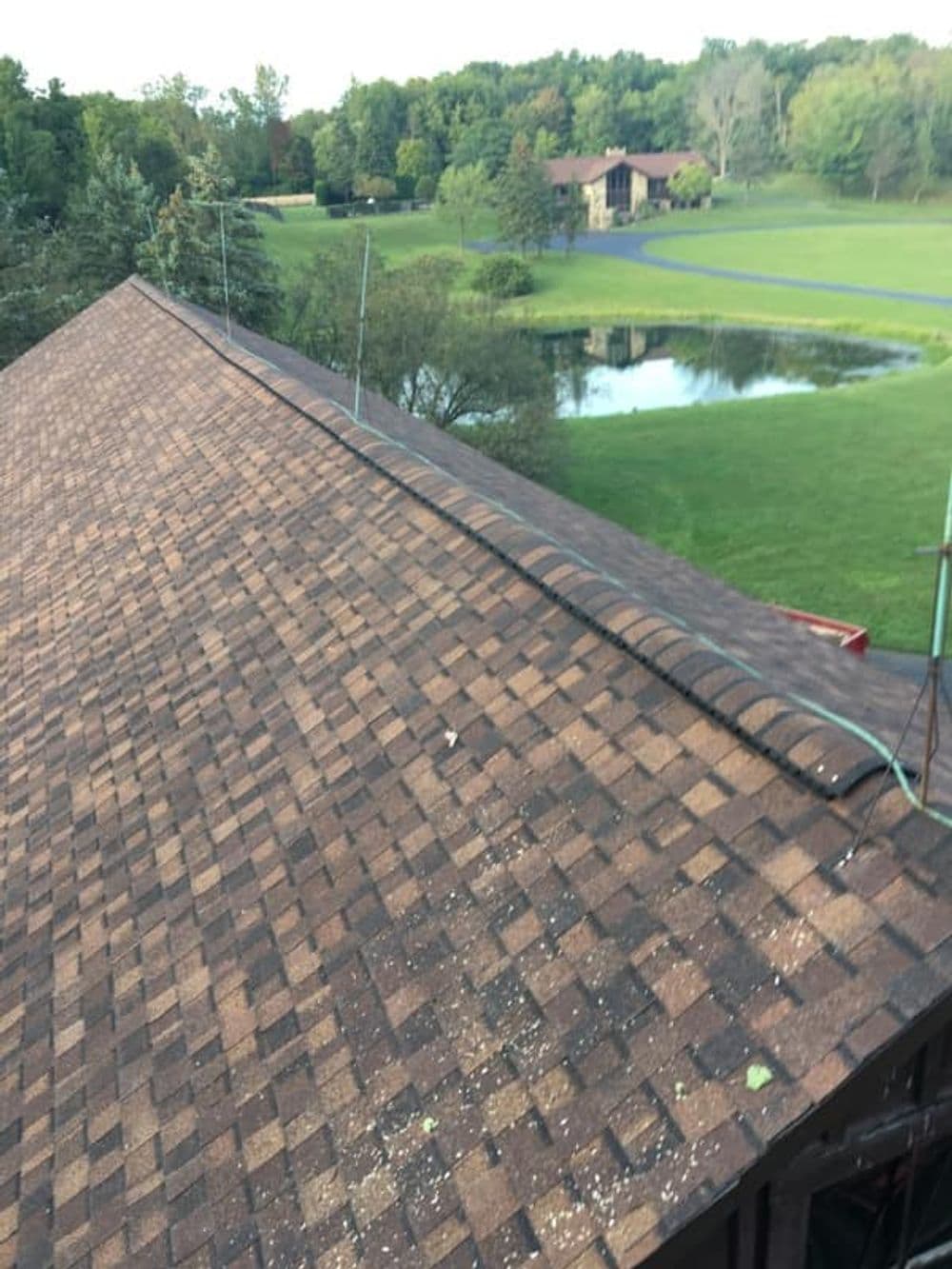 Brown shingle roof with lush green landscaping and a pond in the background.