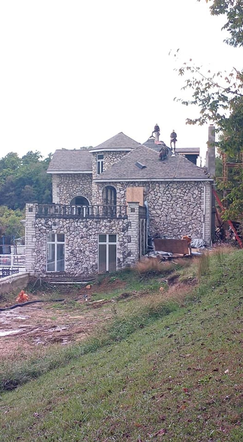 Workers renovating a stone house with a view of the surrounding landscape.