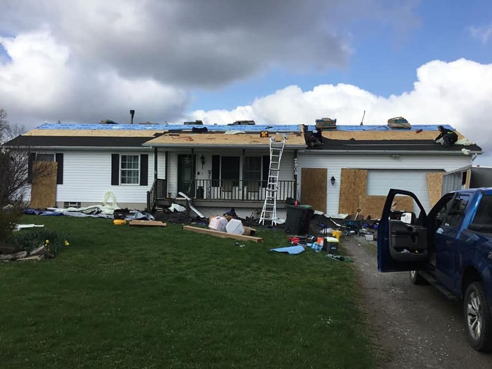 Home undergoing roof repairs with ladders, equipment, and debris visible in front yard.