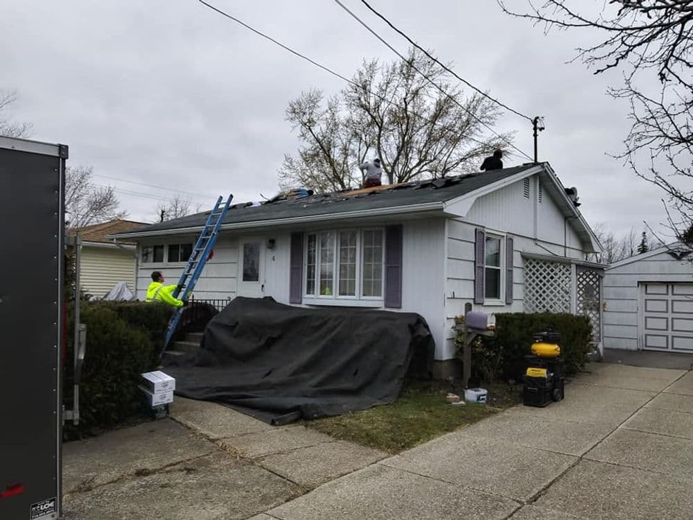 Roof repair in progress on a suburban home with workers and equipment on the roof.
