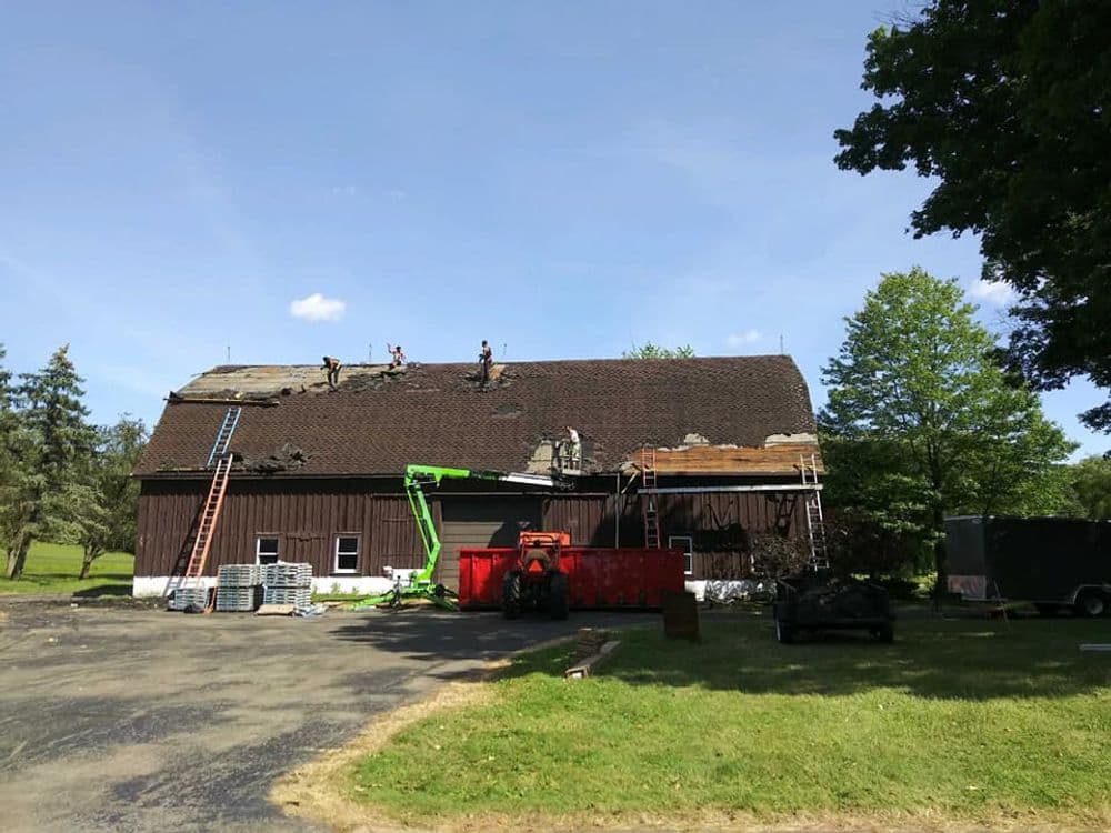 Roof repair on a rustic barn with workers, equipment, and a clear blue sky.