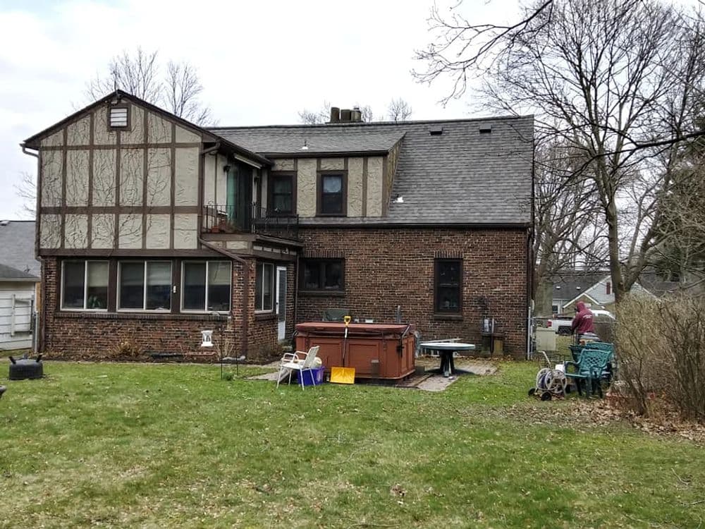 Brick home with a large backyard, hot tub, and outdoor furniture under overcast sky.