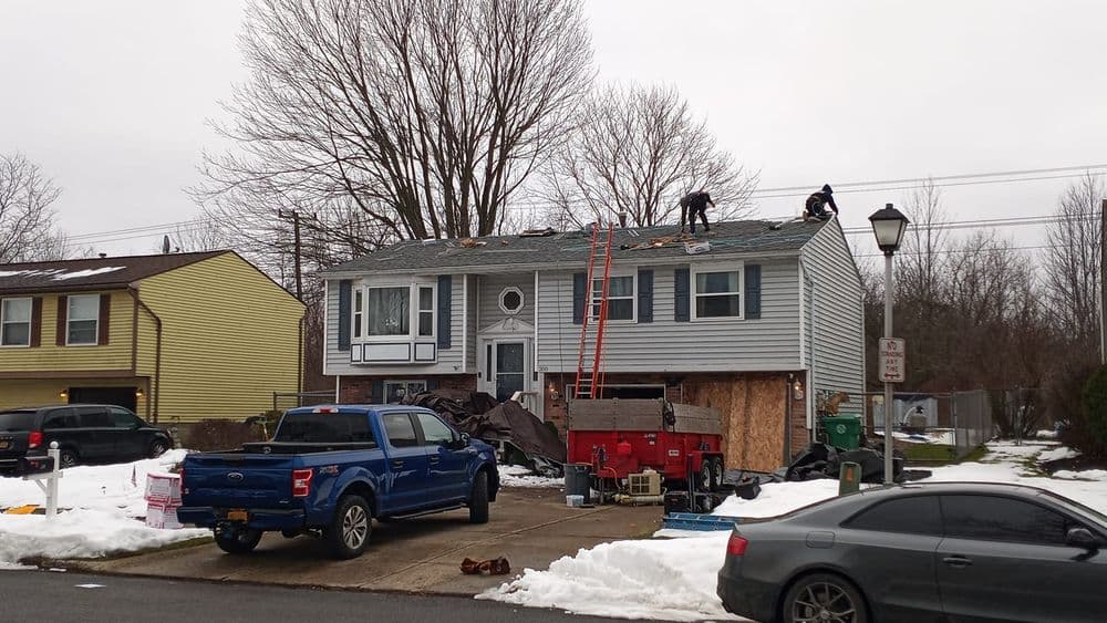 Roofing workers repairing a residential home in winter, with snow on the ground.