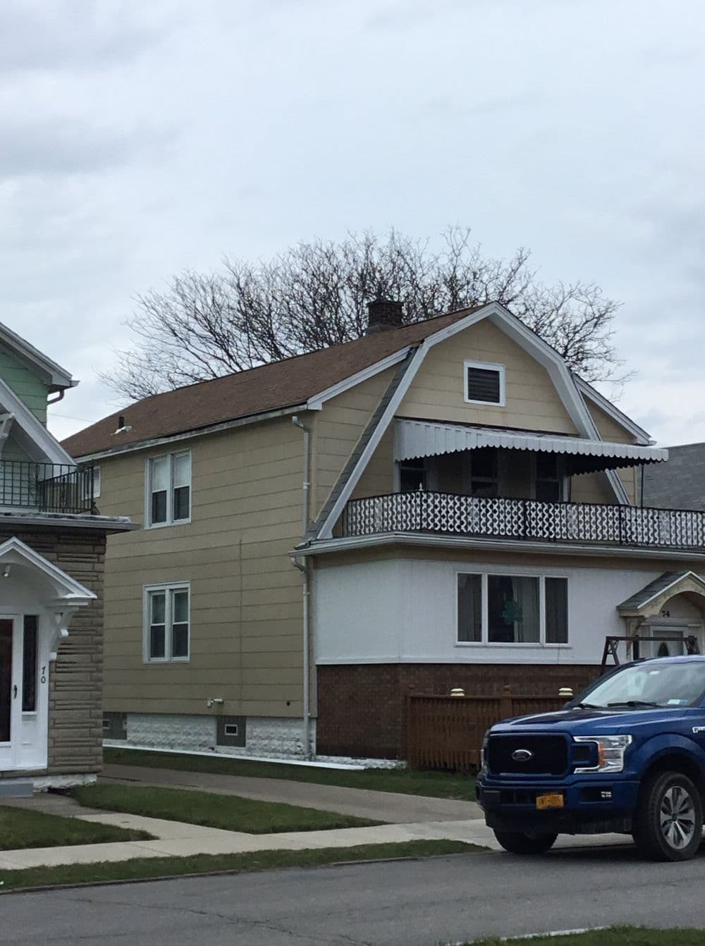 Two-story house with a balcony, surrounded by green lawns and parked blue vehicle.