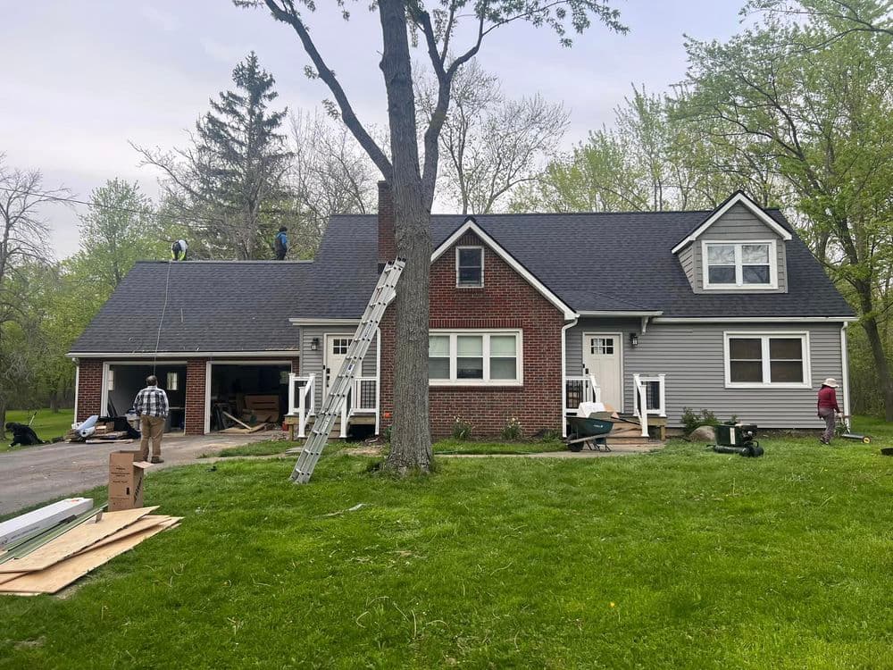 Home renovation in progress with workers installing a new roof and landscaping improvements.