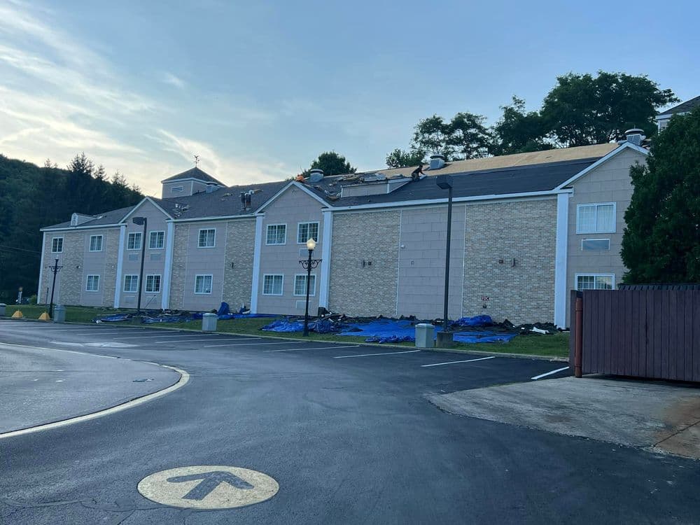 Hotel exterior with visible roof repairs and blue tarps, surrounded by a paved parking area.