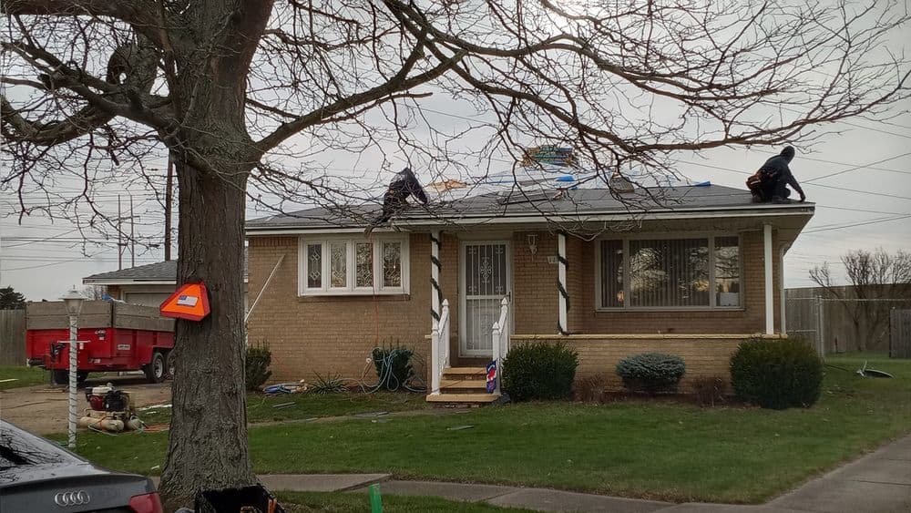 Roofing crew installing new shingles on a suburban home, with tools and equipment visible.
