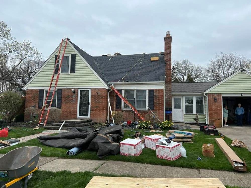 Home exterior undergoing roofing renovation with ladders, tools, and construction materials.