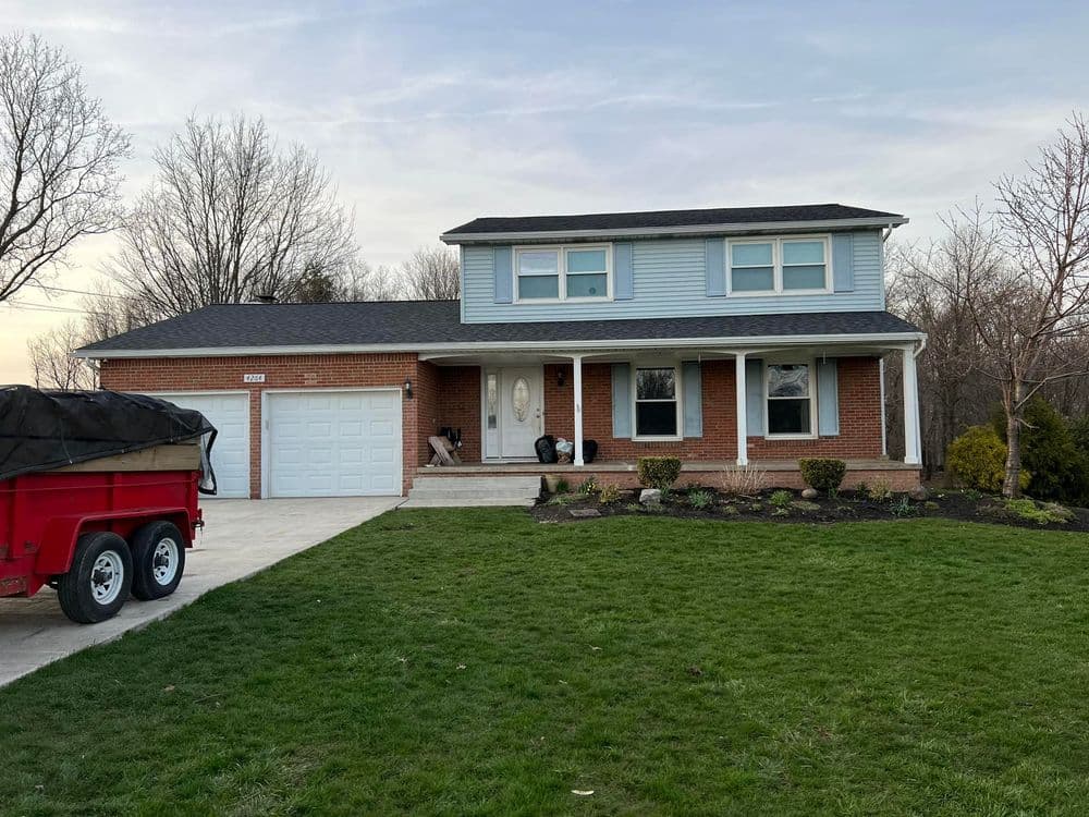 Two-story blue home with red brick facade, porch, and green lawn, featuring a driveway and garage.