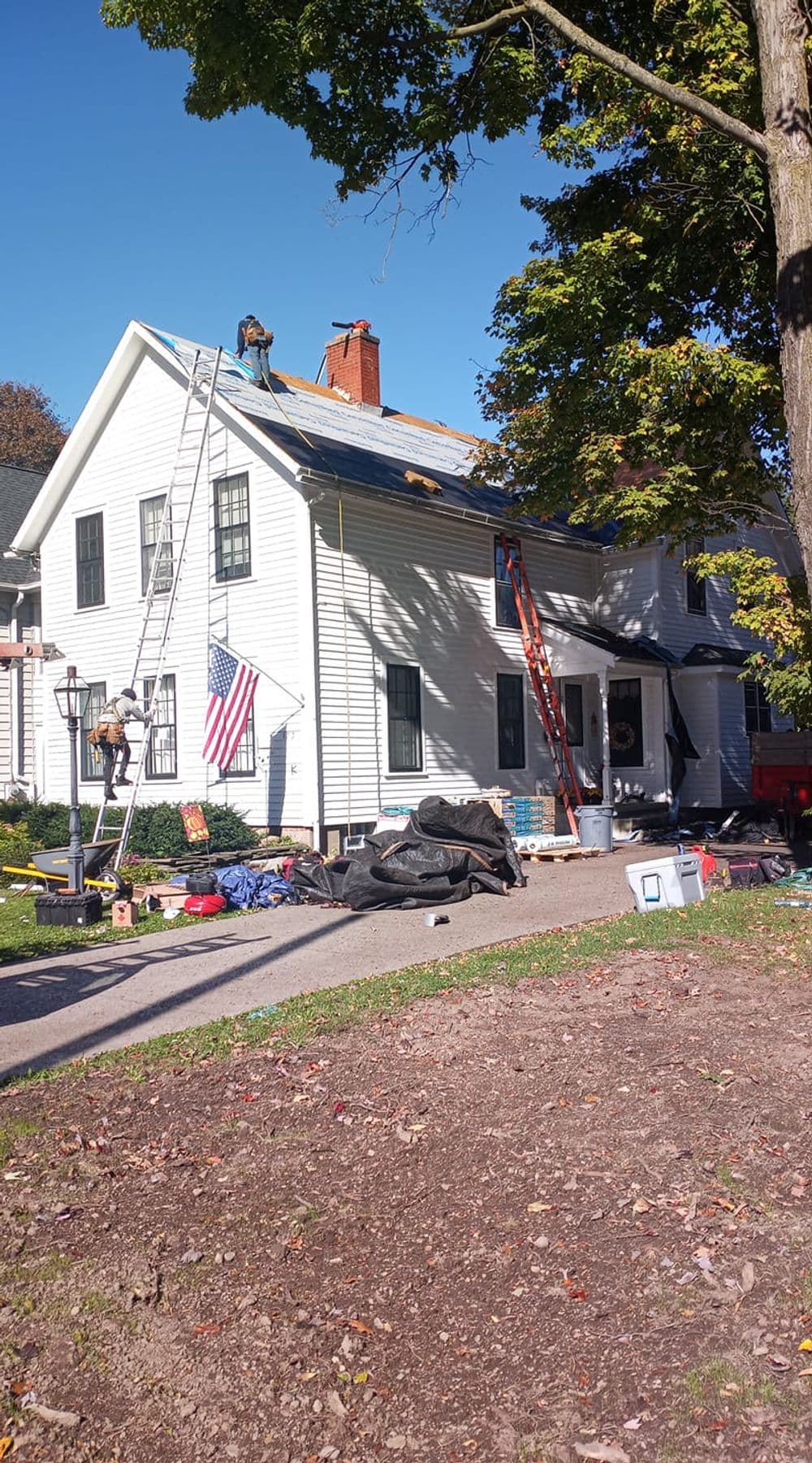 Roofing crew repairing a house with ladders, tools, and an American flag displayed.