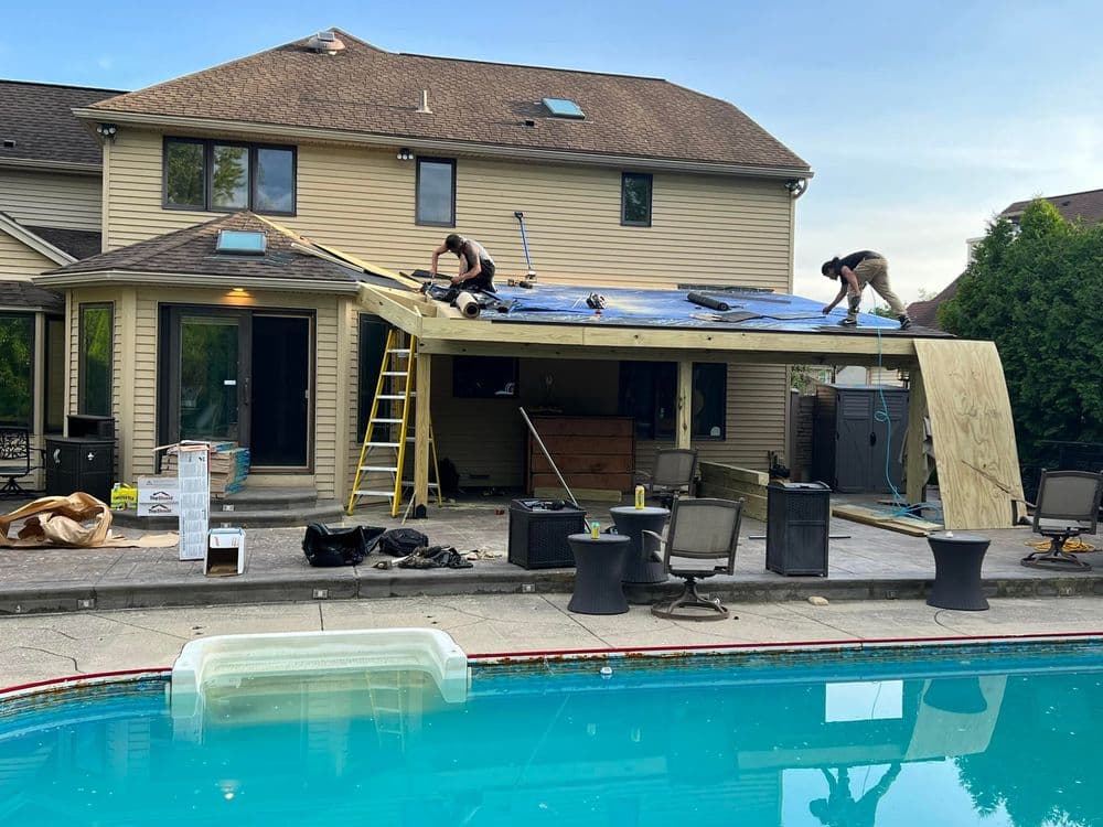 Roof installation on a home extension with workers and pool in the foreground.