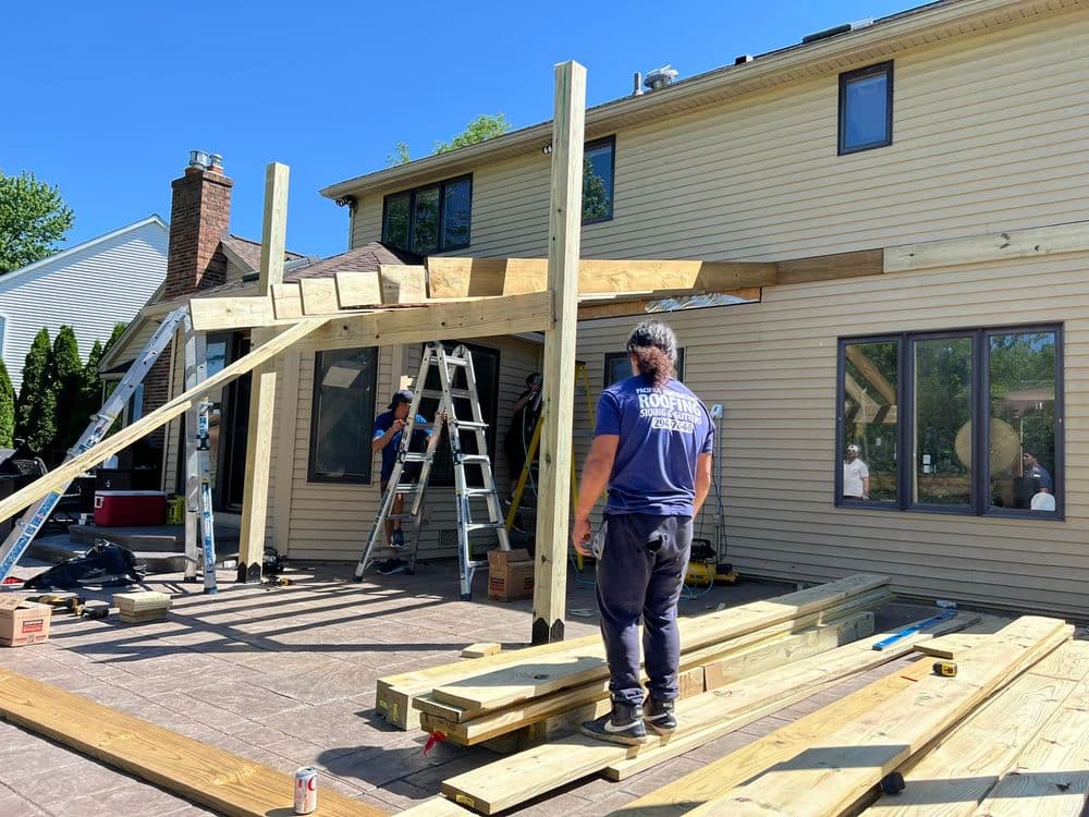 Construction crew building a wooden deck frame outside a house on a sunny day.