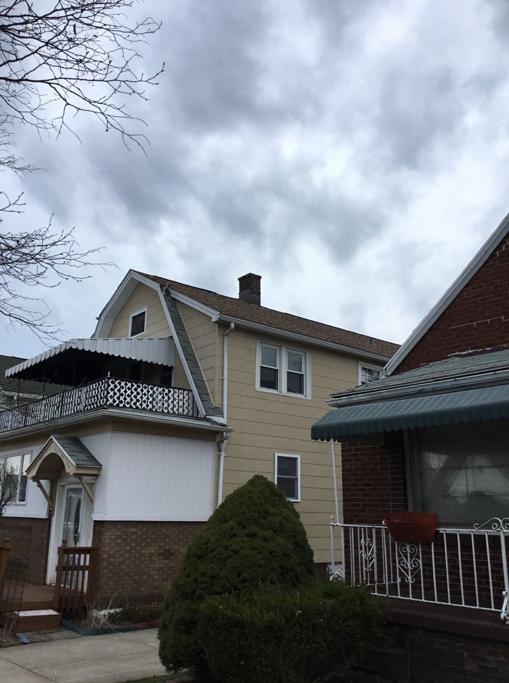 Residential houses under a cloudy sky, featuring a balcony and greenery in the foreground.