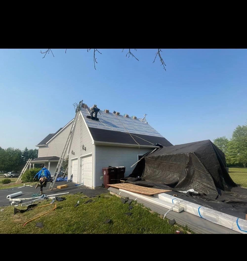 Roof repair in progress on a residential house, with workers and equipment visible.