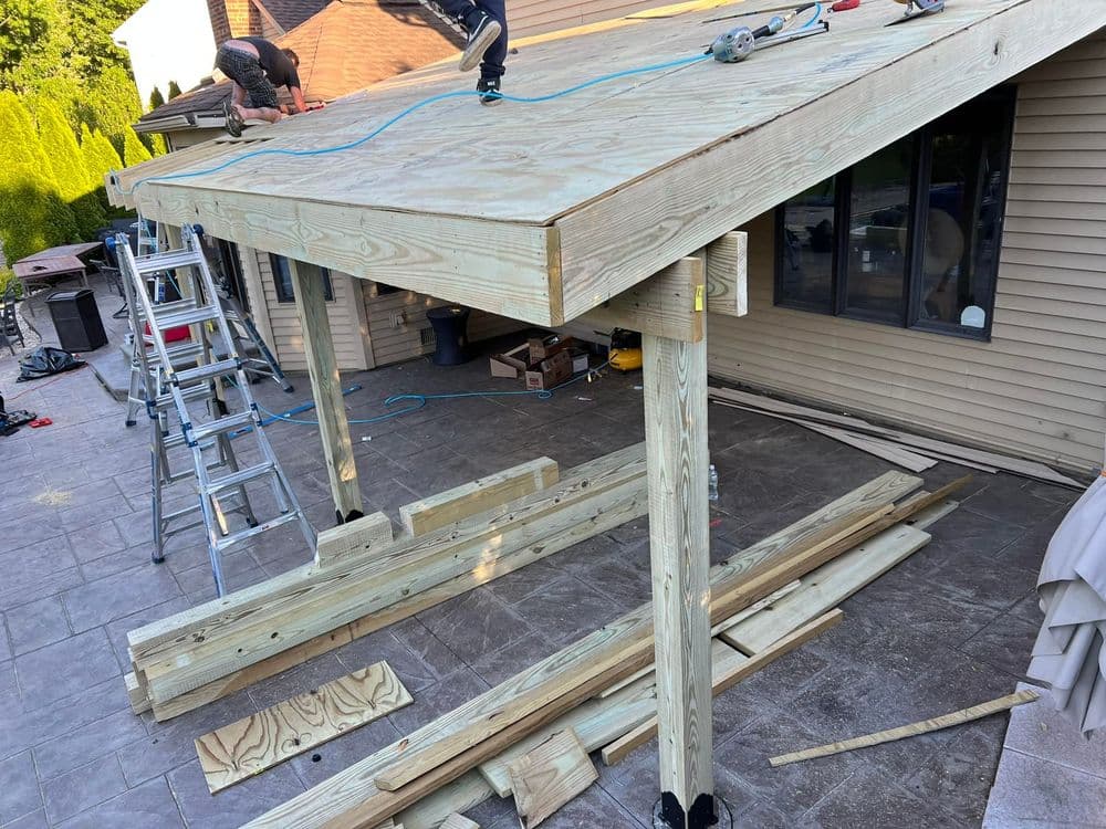 Construction workers assembling a wooden patio roof on a residential home outdoors.