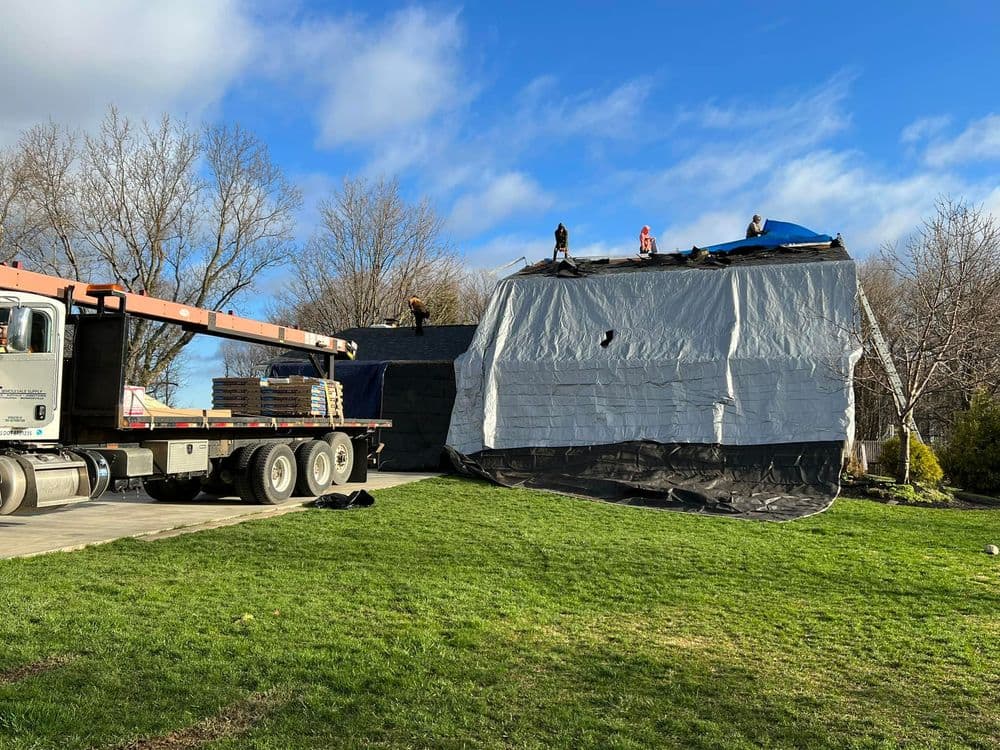 Truck delivering roofing materials for home renovation with workers on the roof.