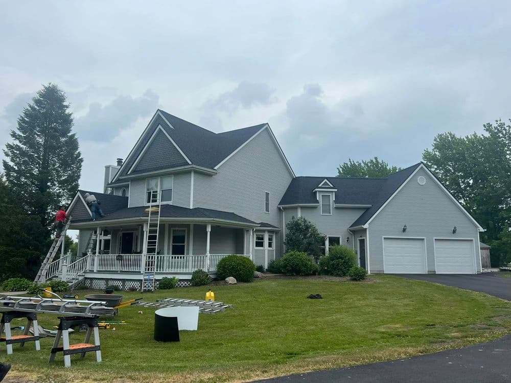 Gray two-story house with a large porch, landscaped yard, and construction work in progress.