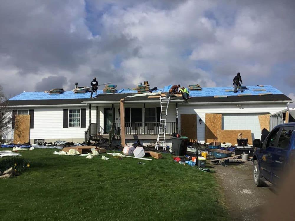 Roof renovation in progress with workers installing shingles on a white house.