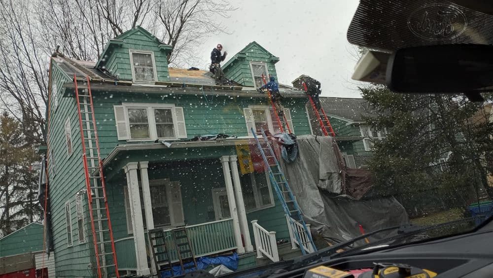 Workers installing a new roof on a green house, with ladders and construction materials visible.
