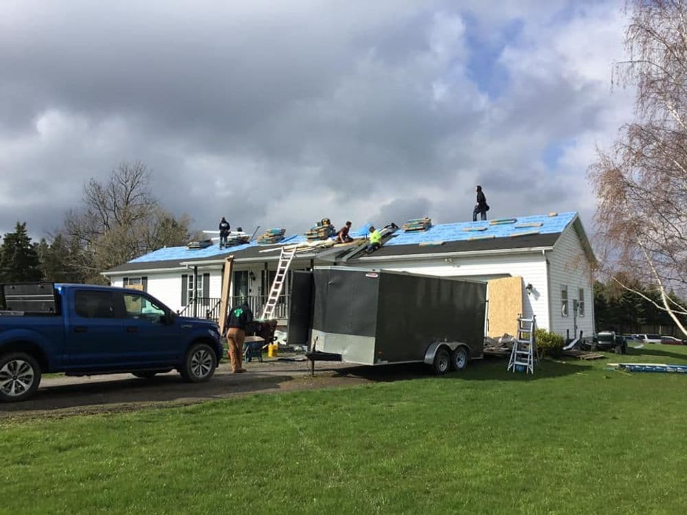 Roofing crew installing new shingles on a residential home with a blue truck nearby.