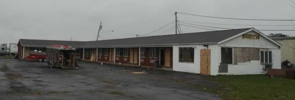 Abandoned motel with boarded windows and a parking area under overcast sky.
