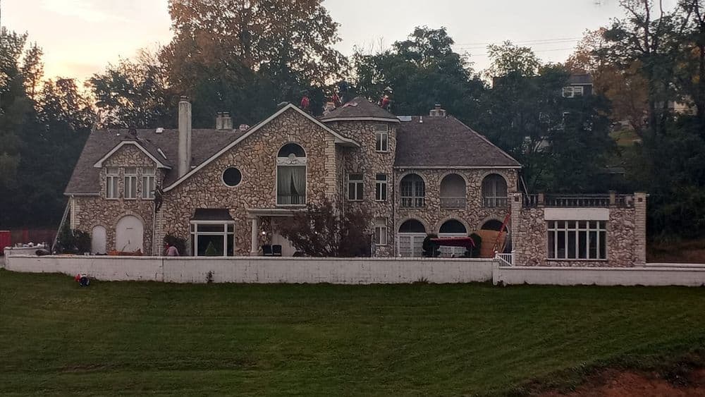 Stone mansion with unique architecture, surrounded by trees and a lawn at sunset.