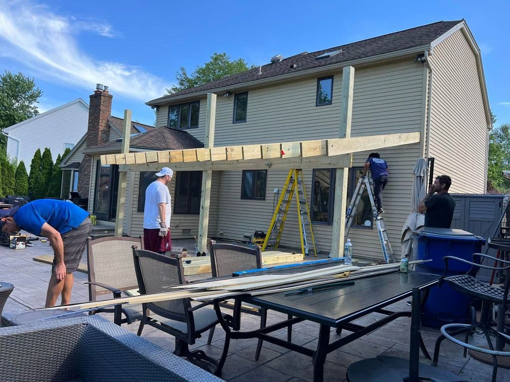 Construction workers building a wooden deck on a residential home, with tools and materials nearby.