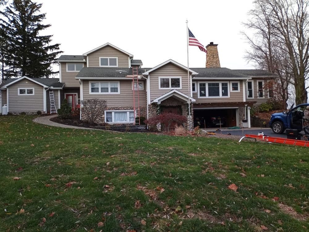 American flag flies over a spacious suburban home with landscaping and a driveway.